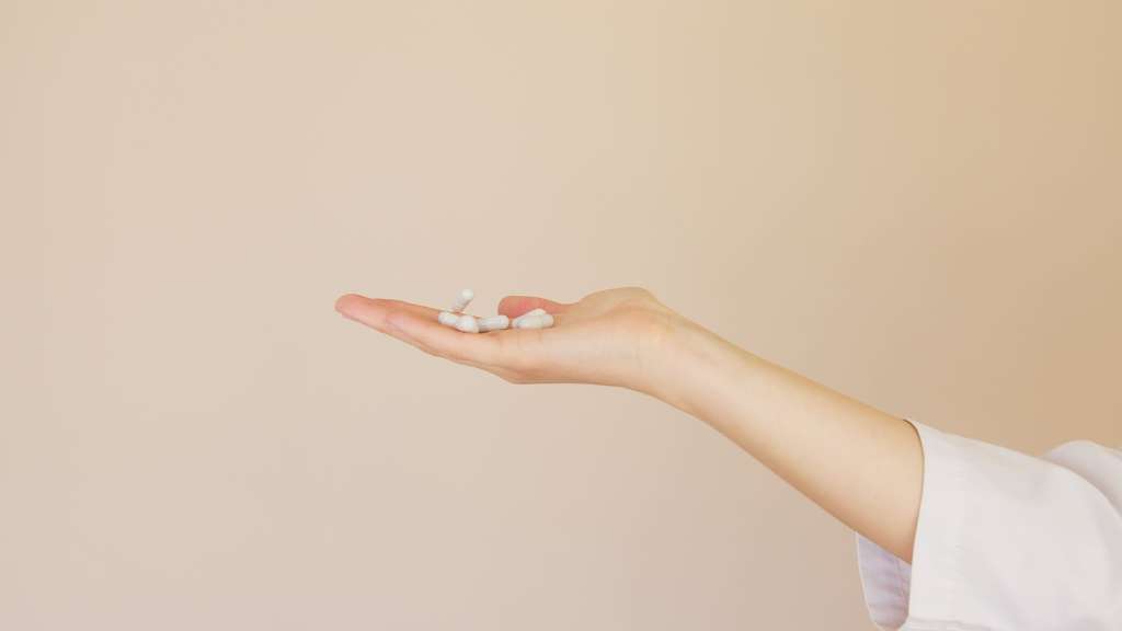 crop female pharmacist with pile of white pills on palm
